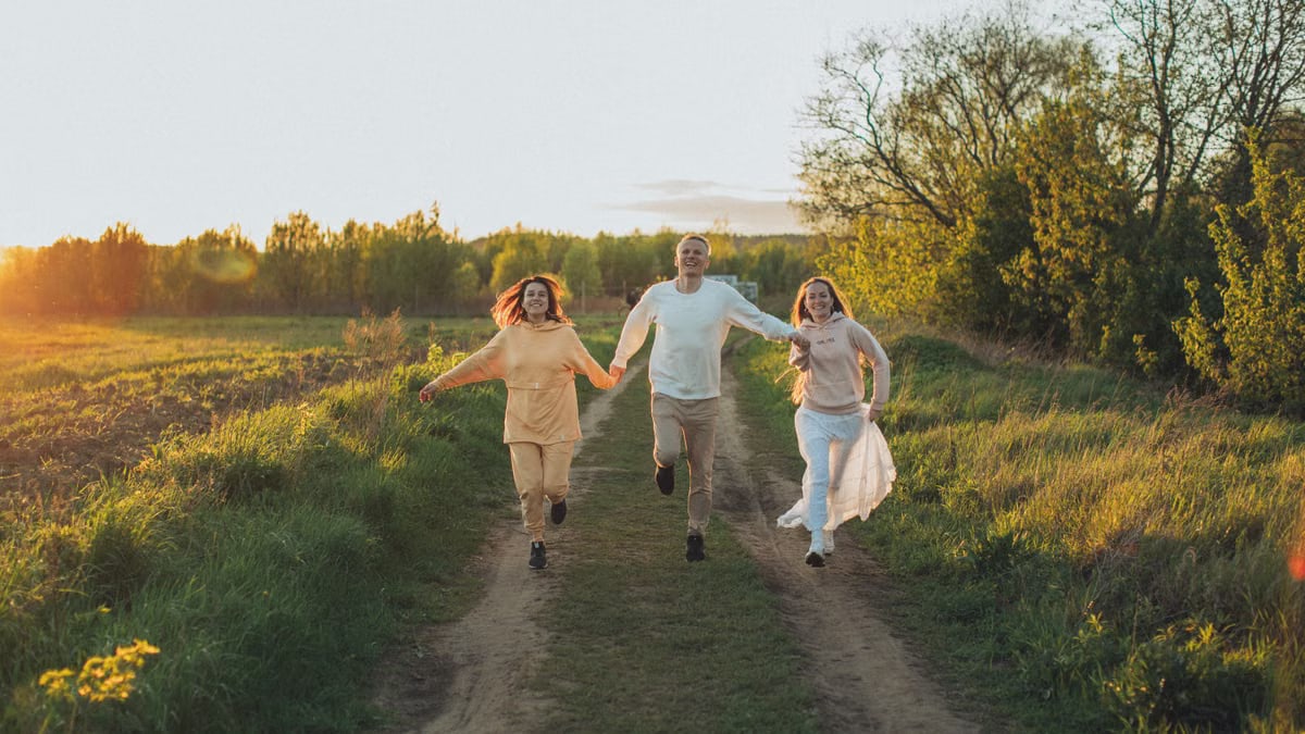 Full body of excited young friends smiling while running together with holding hands towards camera
